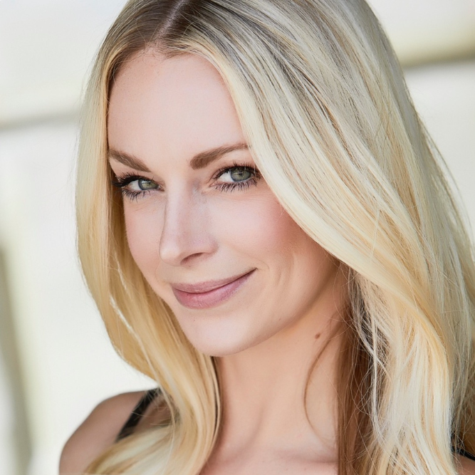 A woman with long, straight blonde hair and light eyes is smiling softly at the camera. She is wearing natural makeup and a sleeveless top, with a blurred, light-colored background.