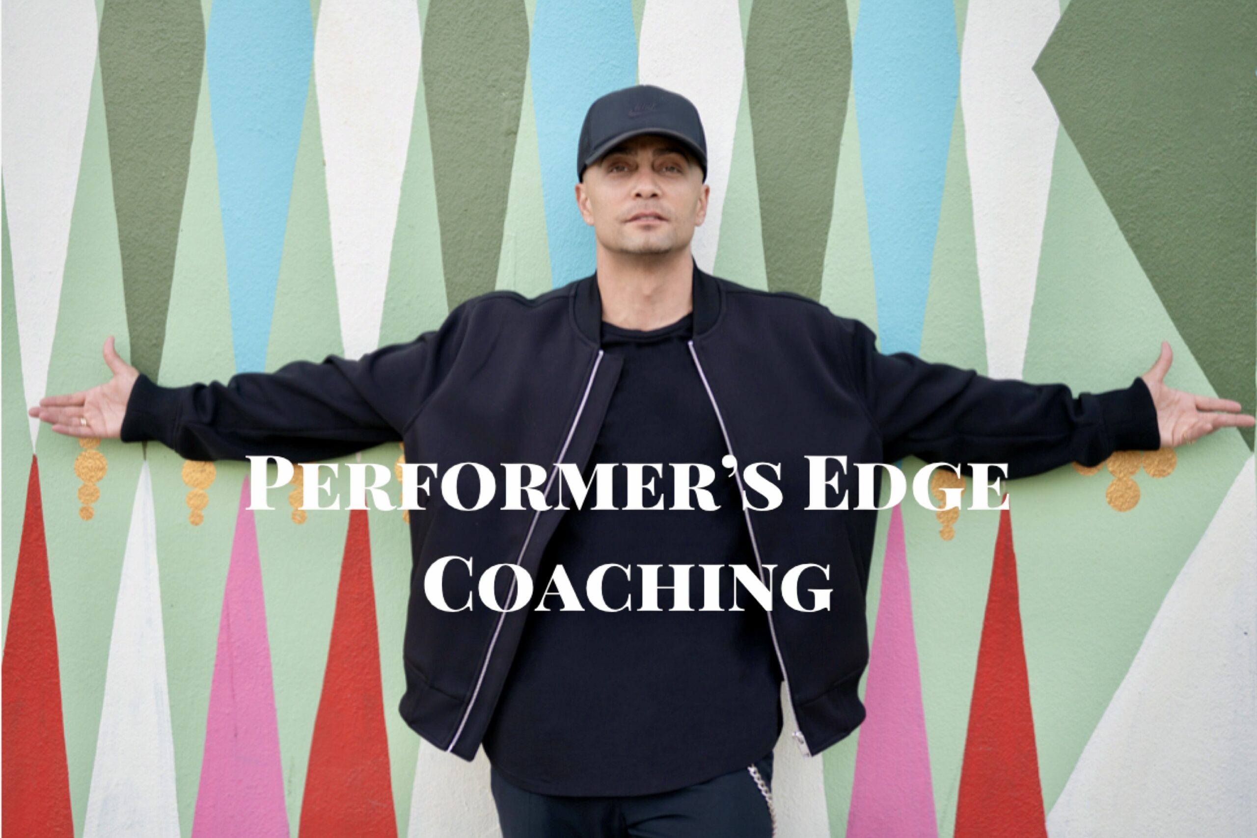 A man in a black cap and jacket stands with arms outstretched in front of a colorful geometric mural. White text across the image reads, Performer’s Edge Coaching.